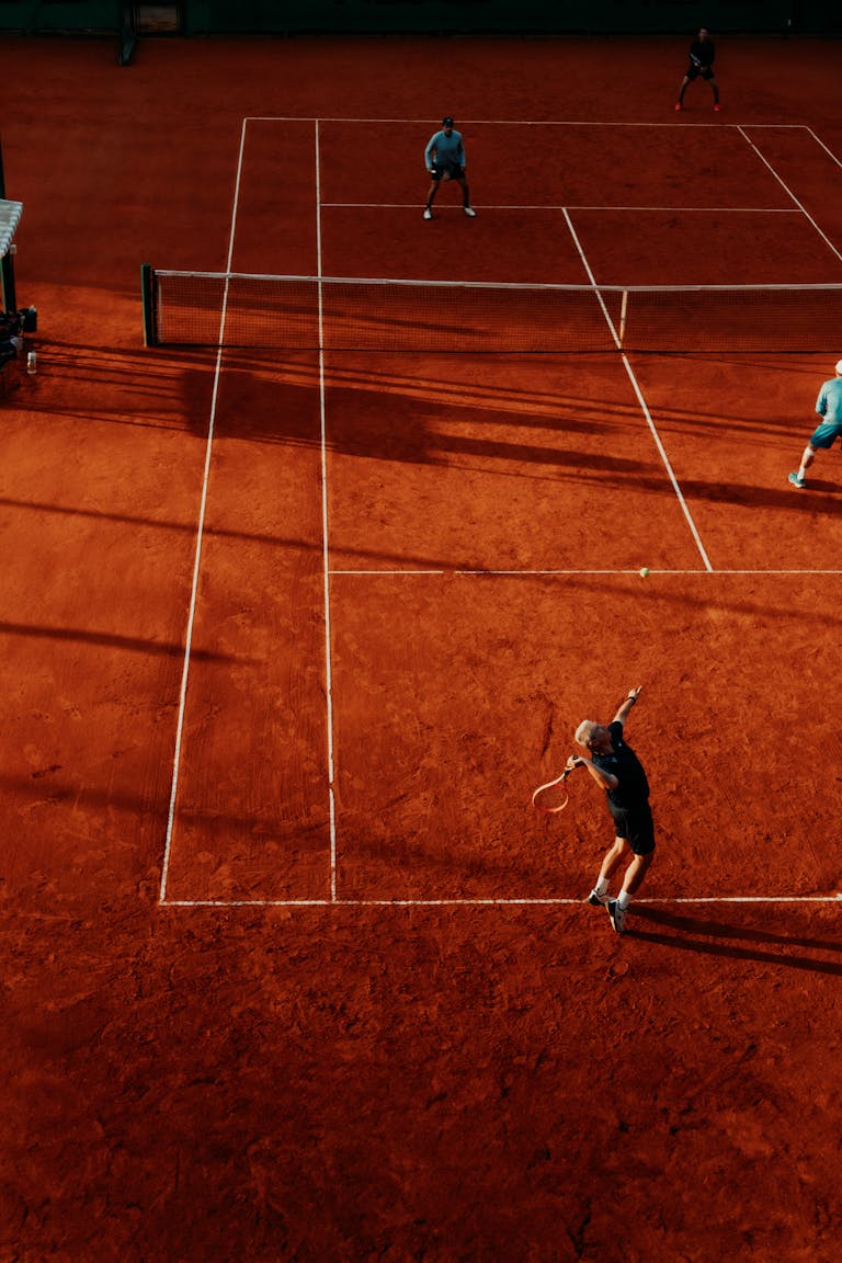 Overhead view of a tennis match on a clay court with four players competing in doubles.